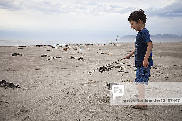 Ein kleiner Junge schreibt seinen Namen in den Sand  während er am Rockaway Beach  Oregon  Urlaub macht.