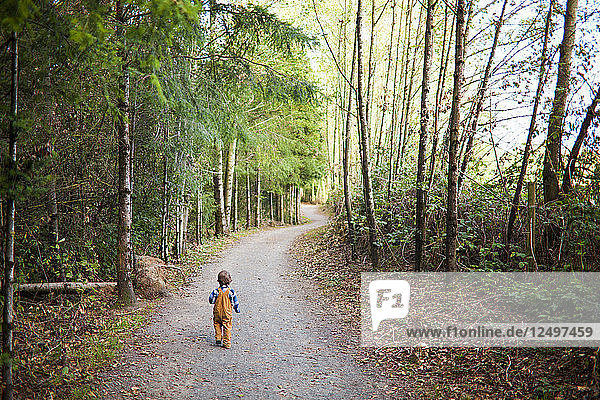 A lonely young boy walks along a gravel pathway at a local park.