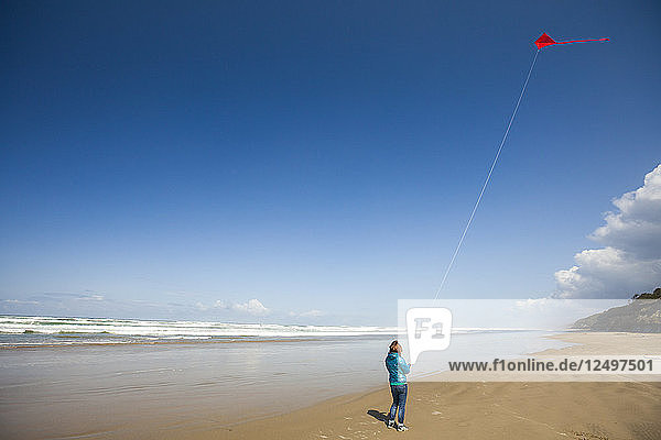 Eine junge Frau lässt einen roten Drachen in den Himmel steigen  während sie einen Strand an der Küste von Oregon besucht