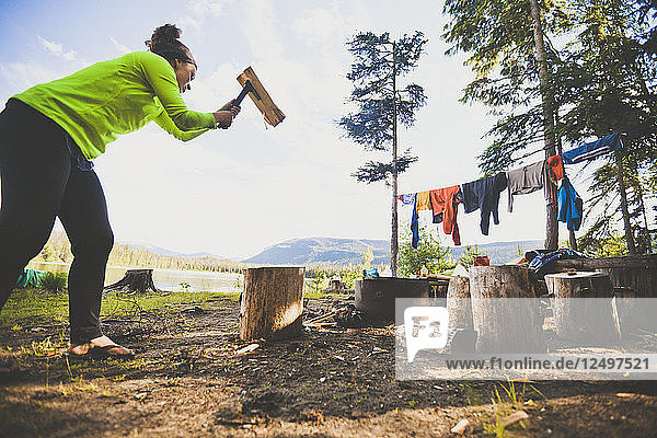 Eine junge Frau hackt mit einer kleinen Axt Brennholz beim Zelten am Unna Lake im Bowron Lake Provincial Park.