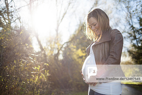 Outdoor portrait of a beautiful young pregnant woman holding her baby bump.