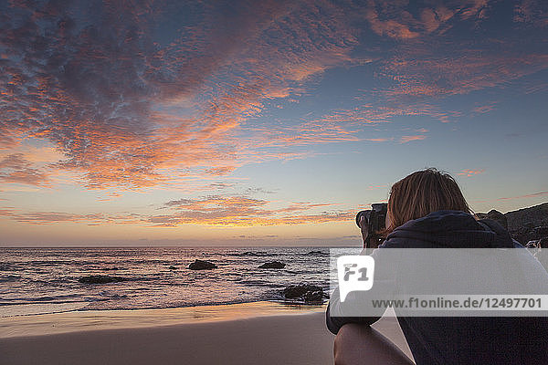 Mädchen (20-30 Jahre alt)  das den Sonnenuntergang vom Strand aus fotografiert  ganz in der Nähe des Ufers. Fuerteventura  Kanarische Inseln