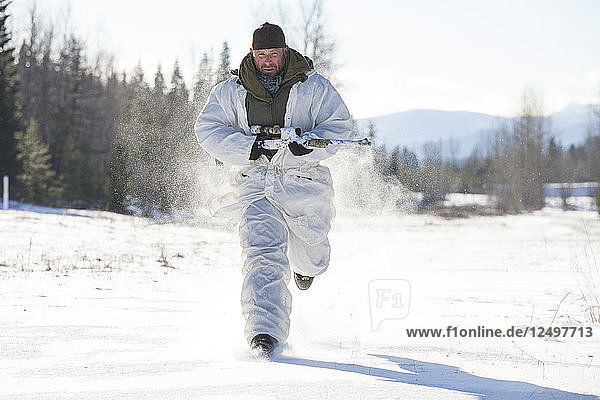 A hunter wearing a cold-weather camouflage outfit carries his rifel while running through a snow-covered field in British Columbia  Canada.