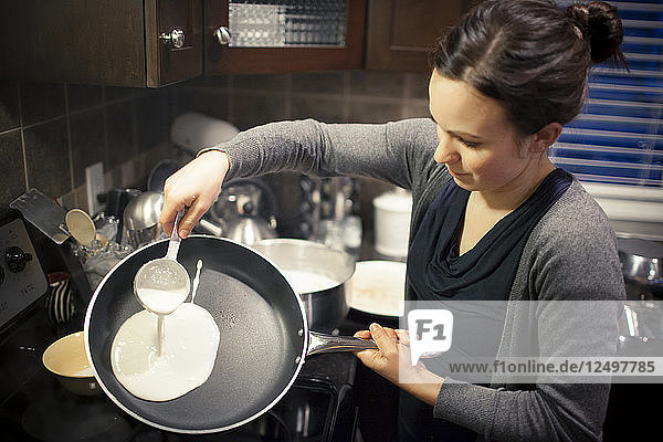 A young woman prepares crepes in her kitchen.