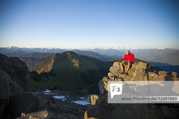 Ein Mann arbeitet an einem Tablet  während er auf dem Gipfel des Sauk Mountain in Washington sitzt.