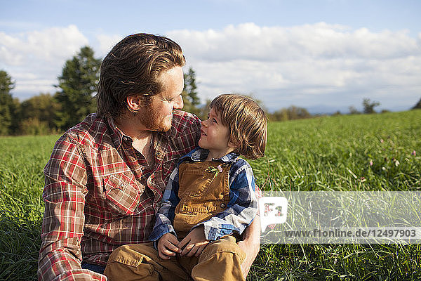 Porträt eines Vaters und seines Sohnes im Freien  die einen intimen Moment miteinander verbringen  während sie auf einer Wiese sitzen.