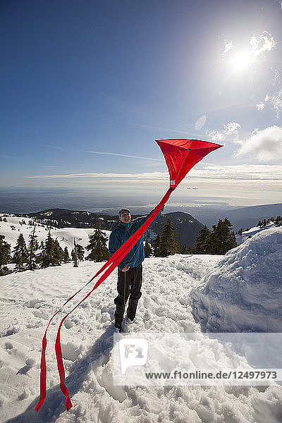 Happy Man Flying A Kite On The Top Of A Snow Covered Mountain