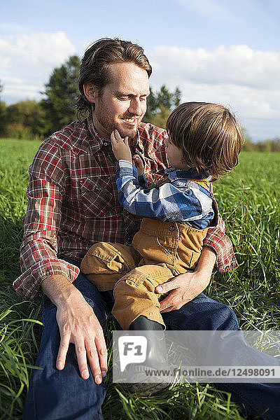 Ein Vater sitzt mit seinem kleinen Sohn zusammen  während der Sohn mit seinem Bart spielt.