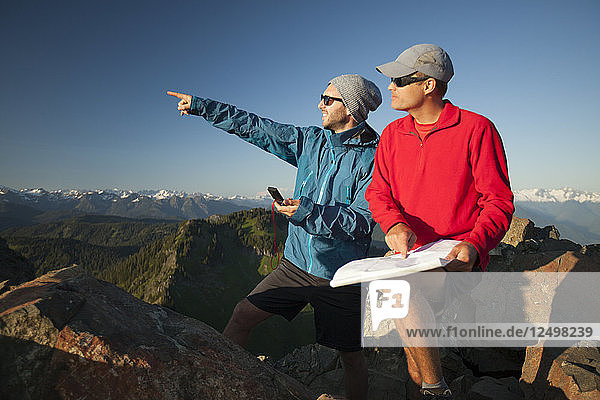 Zwei Männer benutzen eine Papierkarte und einen Kompass  um beim Wandern in der North Cascade Mountain Range nahe gelegene Gipfel zu identifizieren.