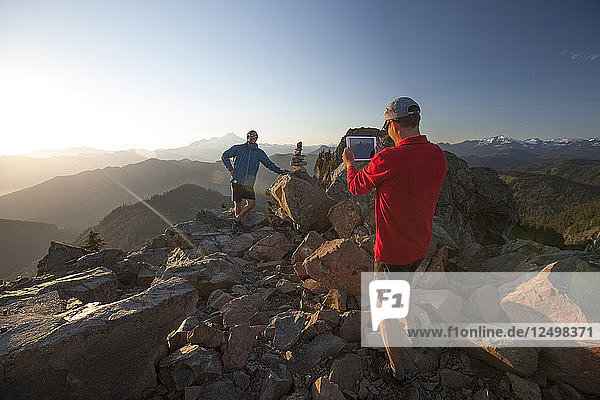 Ein Mann macht mit einem Tablet ein Foto von seinem Freund auf dem Gipfel des Sauk Mountain in Washingotn.