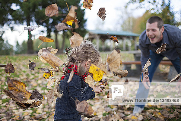 Ein Vater und eine Tochter spielen mit Herbstblättern im Park