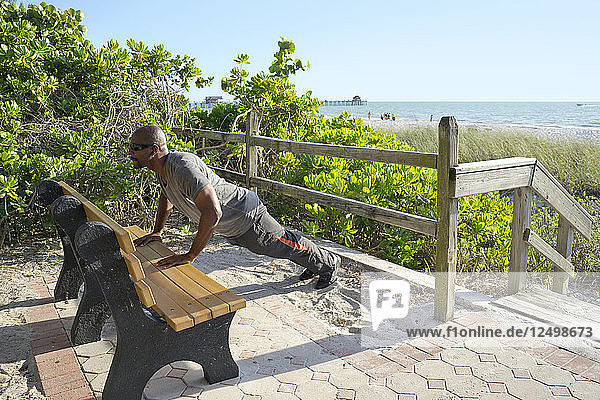 Man doing push ups on a park bench at the beach