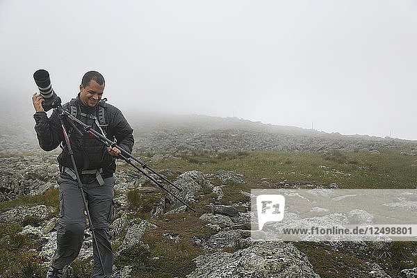 Mann mit der Kamera auf dem Gipfel des Mount Washington bei starker Bewölkung