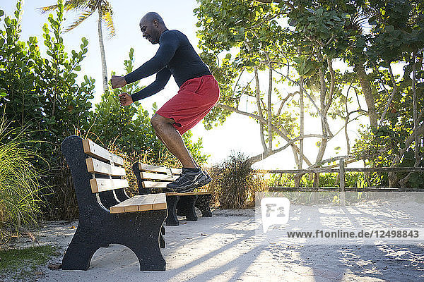Man exercises by jumping up on a park bench in a tropical setting