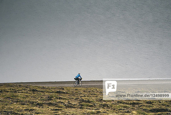 Ein Radfahrer fährt entlang der Küste mit dem Meer im Hintergrund in der Nähe von Holmavik  Island