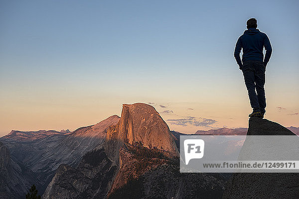 Mann auf einem Felsen stehend mit Blick auf den Half Dome im Licht des Sonnenuntergangs. Yosemite  CA  USA.