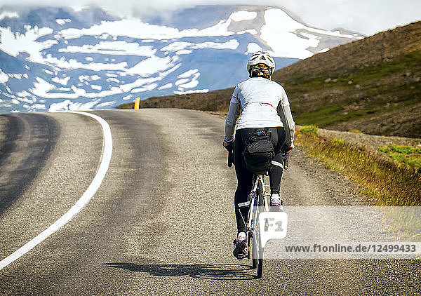Ein Radfahrer fährt über den Gipfel einer Steigung mit schneebedeckten Bergen im Hintergrund