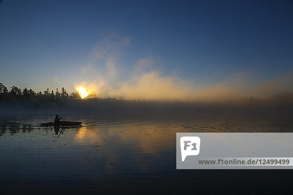 Ein Kajakfahrer genießt den Sonnenaufgang  während an einem kühlen Herbstmorgen Dampf aus dem Lake Pleasant in Conover  Wisconsin  aufsteigt.
