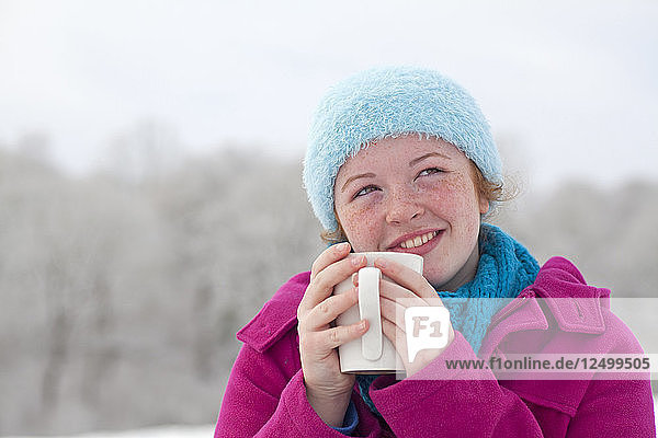 Teenage girl enjoying a Hot Chocolate outside in the snow in winter UK.