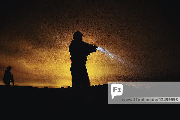 Silhouette of person in military uniform with weapon and flashlight