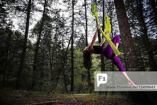 Eine Frau praktiziert Luft-Yoga im Wald.