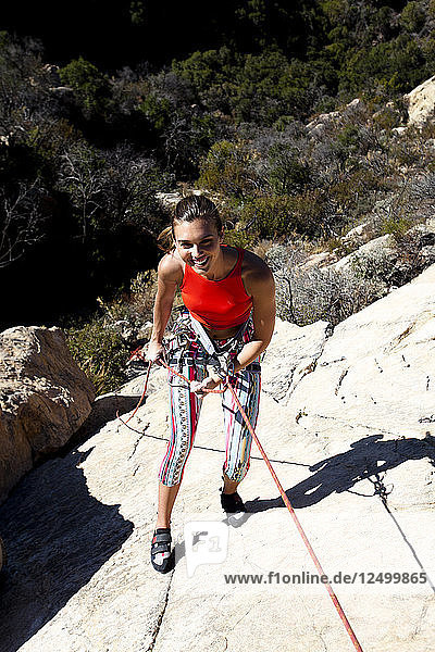 A woman wearing a red tank top and striped pants rappels Lower Gibraltar Rock in Santa Barbara  California