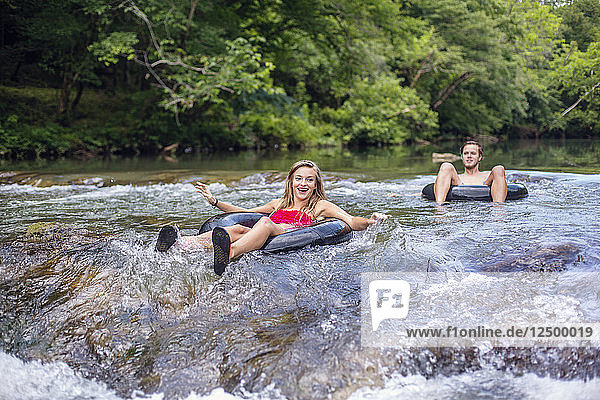 A young woman smiles while anticipating going over rapids in a tube on a river.