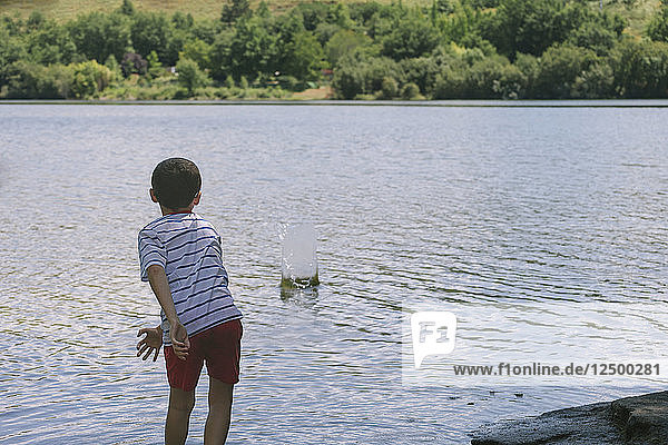 Boy throws rock and plays alone by a lake during summer.