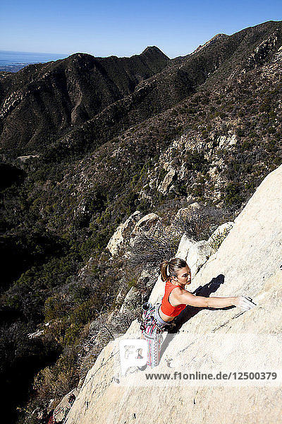 Eine Frau mit rotem Tanktop und gestreifter Hose klettert The Rapture (5.8) am Lower Gibraltar Rock in Santa Barbara  Kalifornien. The Rapture ist eine sehr schöne und unglaublich gut abgesicherte Route auf der linken Seite des Lower Gibraltar Rock.