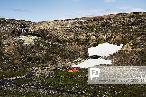 Distant View Of Two Tents Beneath Snowfields And Waterfalls In Iceland