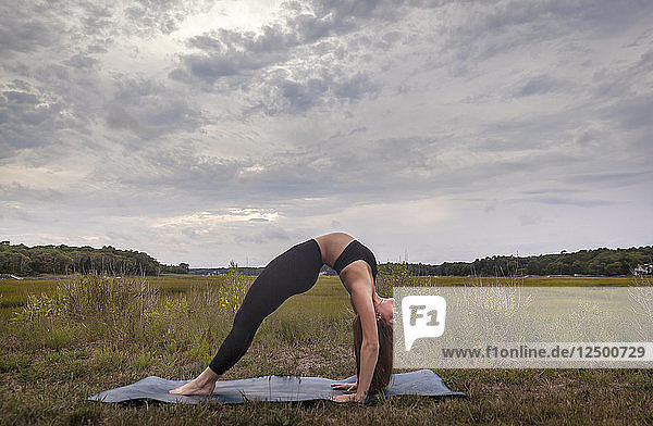 Schöne junge Frau in Rad-Pose auf einer Yoga-Matte bei Sonnenuntergang