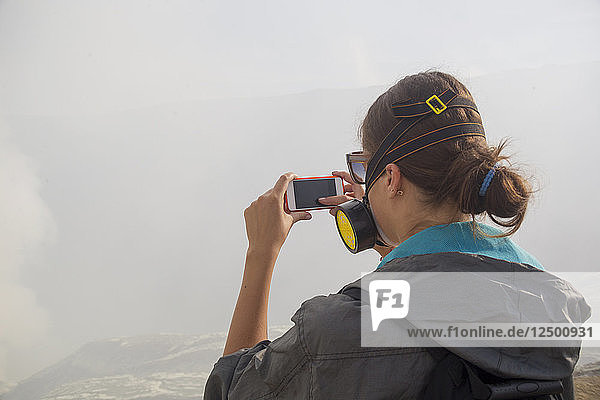 Junge Frau nimmt Bild mit Handy in Vulkan Kawah Ijen