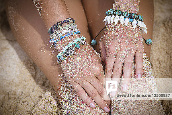 Weibliche Hand mit Armbändern am Strand.