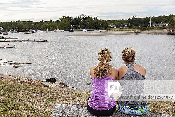 Zwei Freundinnen sitzen am Wasser und blicken auf den Hafen und tragen Trainingskleidung.