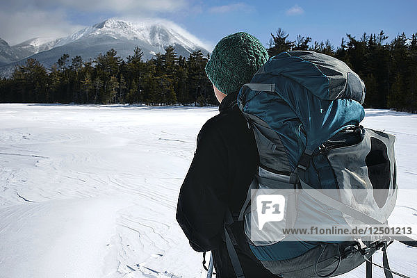Eine junge Frau macht bei einer Schneeschuhwanderung durch den Baxter State Park eine Pause  um einen Blick auf den windgepeitschten Mount Katahdin zu werfen.
