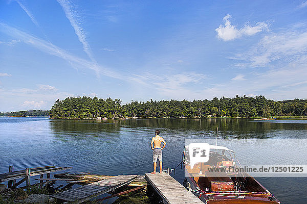 Ein junger Mann  der am Rande eines Docks neben einem hölzernen Boot steht