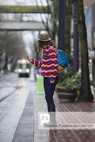 Eine Frau mit einem Mobiltelefon steht an einer Straße und wartet auf einen Zug in Portland  Oregon.