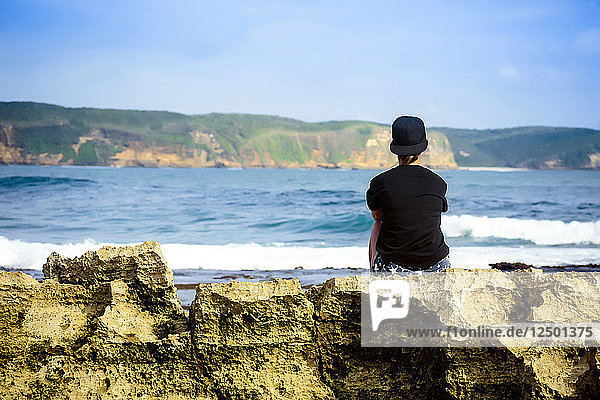 Frau an der Küste sitzend  die Aussicht betrachtend