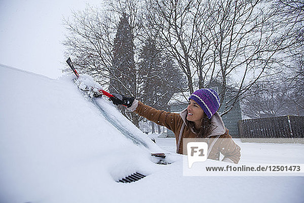 An Adult Woman Clearing Off Her Windshield After A Fresh Blanket Of Snowfall