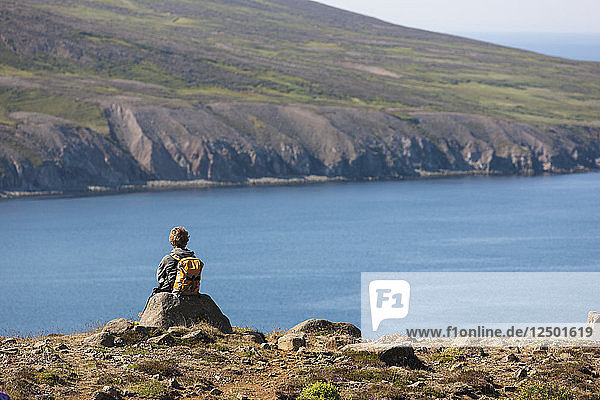 Wanderer  der sich auf einem großen Stein mit Blick auf das Meer am Fjord Thorgeirsfjordur  Nordisland  ausruht.