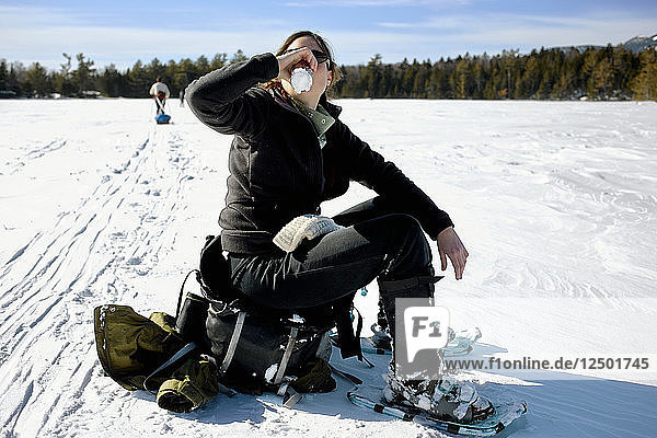 Eine Frau macht nach einer Schneeschuhwanderung durch den Baxter State Park in Maine eine Pause  um ein Bier zu trinken. Sie ruht sich am Daicey Pond aus.