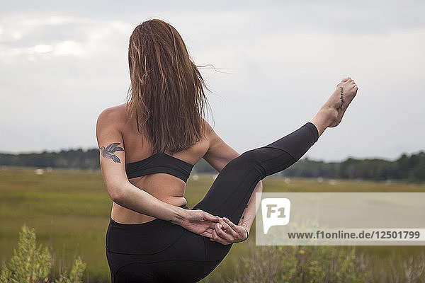 Schöne junge Frau in einer balancierenden Bindung  die Yoga bei Sonnenuntergang macht