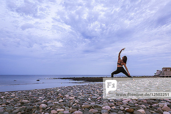 Schöne junge Frau in Reverse Warrior Doing Yoga bei Sonnenuntergang
