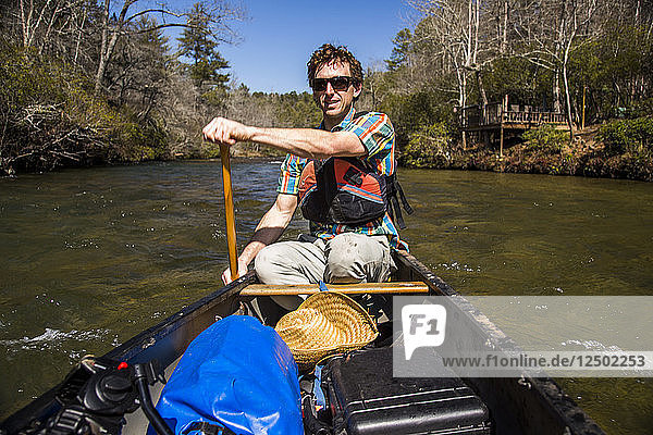 A man paddles a canoe down the calm Chattahoochee River in North Georgia.