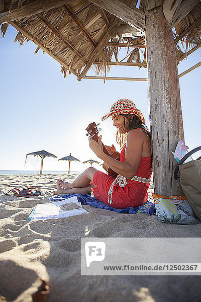 Frau spielt ihre Ukulele an einem Strand unter einer Palapa