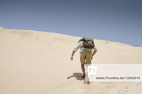 Mann mit Rucksack klettert auf Sanddüne