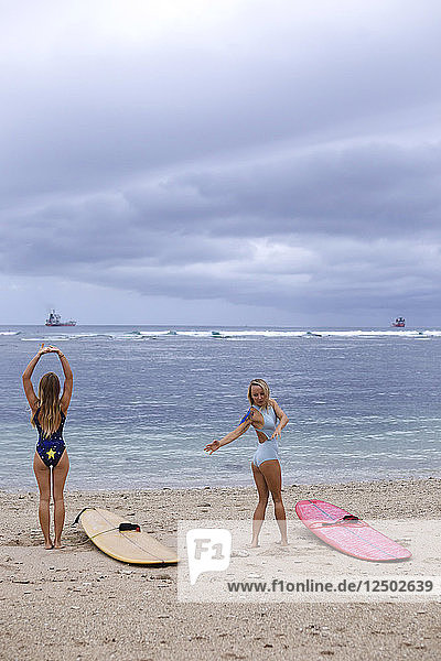 Zwei junge Frauen strecken und beugen sich vor dem Surfen am Strand
