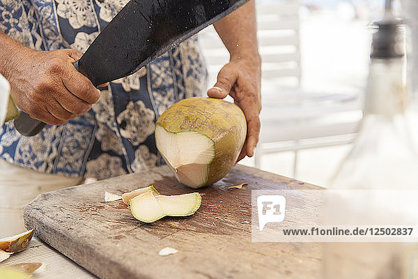 Ein Mann schneidet eine Kokosnuss mit einer Machete  um an die Kokosmilch zu gelangen.