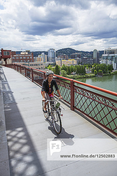 A woman riding over the Broadway Bridge in Portland  Oregon. A view of the city is just beyond.