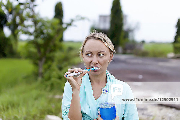 Young woman brushing teeth outdoors